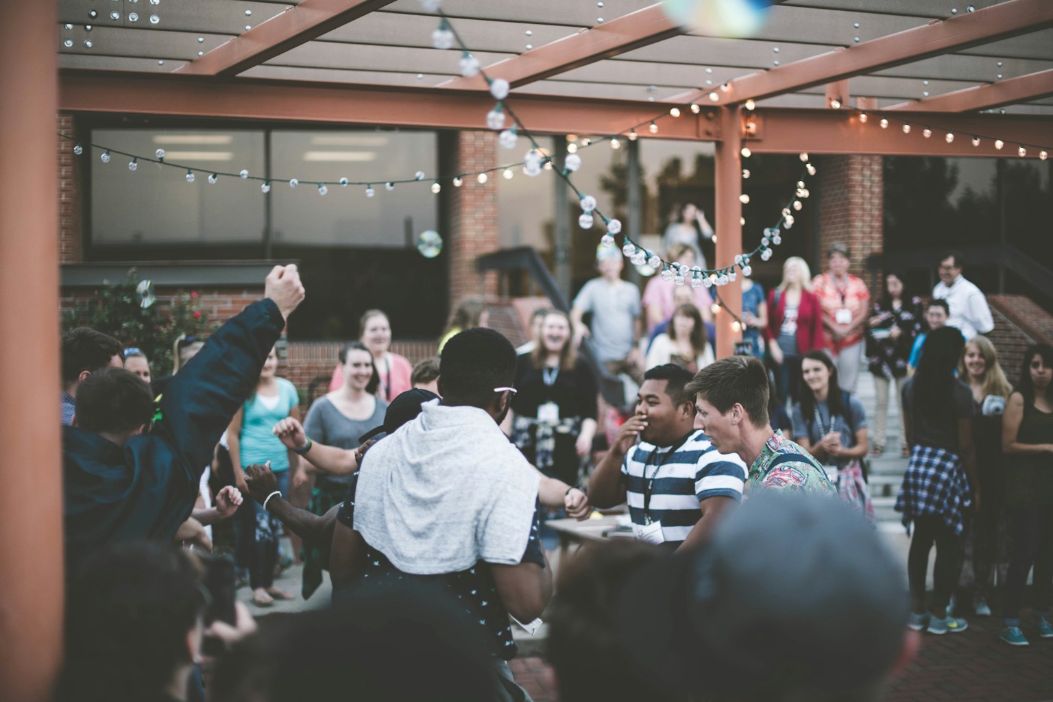 Outdoor community gathering under string lights, people dancing and celebrating together
