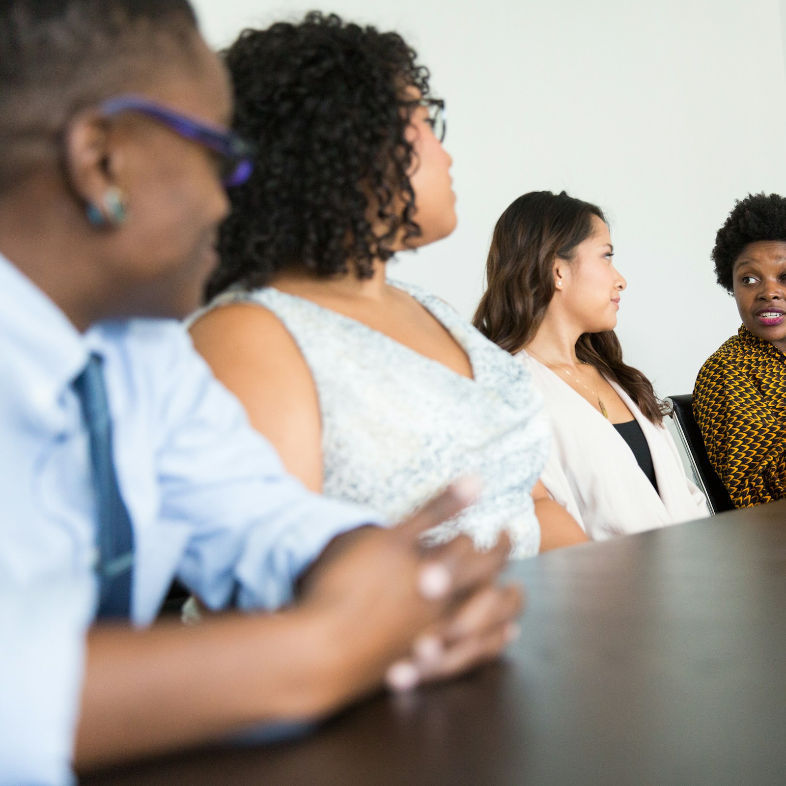 Five Black women in professional dress in conversation around a conference table